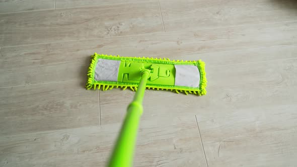 Green microfiber mop moving on the parquet floor to keep the house clean alt