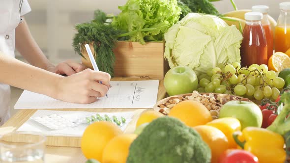 Closeup Dietitian Writes Recommendations for Proper Nutrition Next to a Lot of Vegetables and Fruits