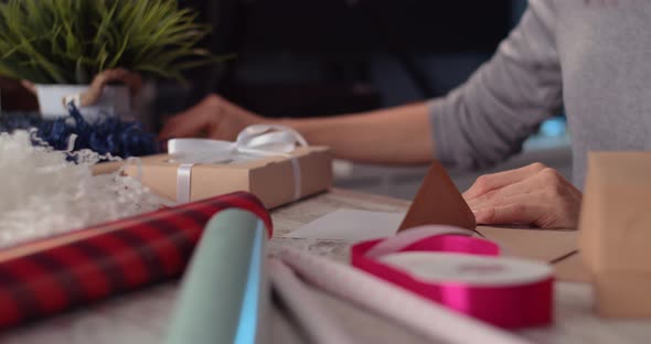 Woman writing postcard and wrapping a gift in living room alt