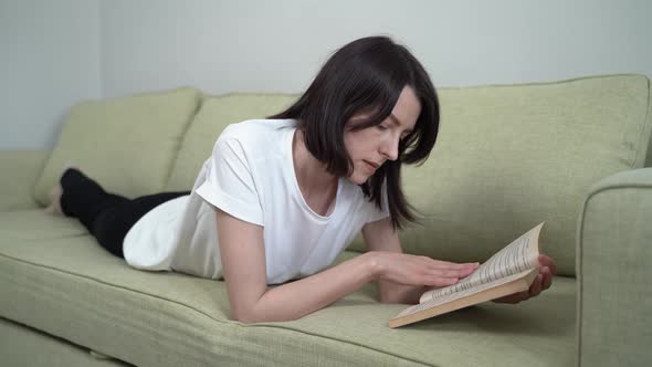 Brunette Woman Reading a Book Lying on the Couch