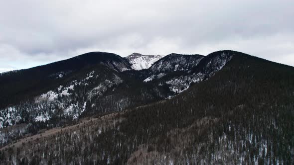 Panning drone shot of a snow covered mountain peak with fasting clouds alt