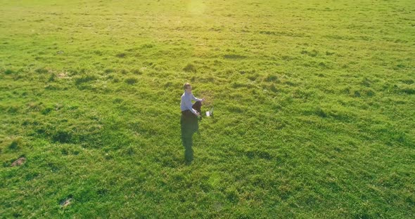 Low Orbital Flight Around Man on Green Grass with Notebook Pad at Yellow Rural Field alt