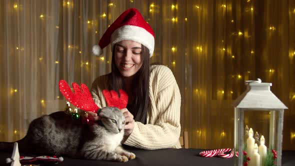 Stylish Happy Girl in Santa Hat Playing with Cute Cat