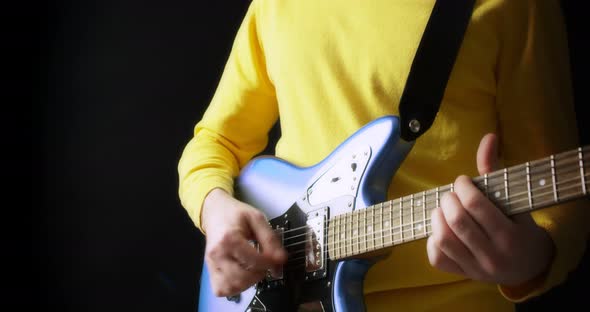 Male Guitarist in a Yellow Jumper Plays an Electric Guitar on Black Background alt