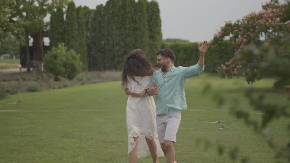 Joyful young couple caught by the sudden sprinkler water in the park