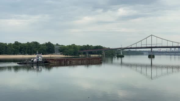 Industrial tugboat towing a long barge with sand, sailing along the fairway of the river at sunset. 