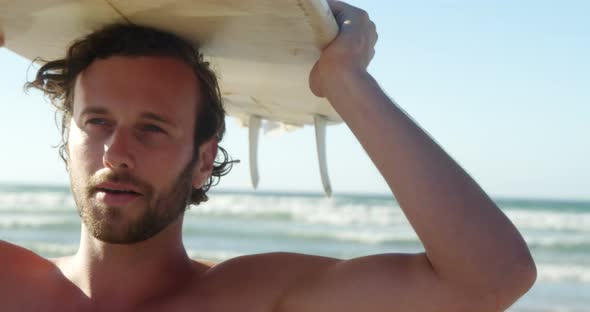 Young man carrying surfboard on head at beach alt