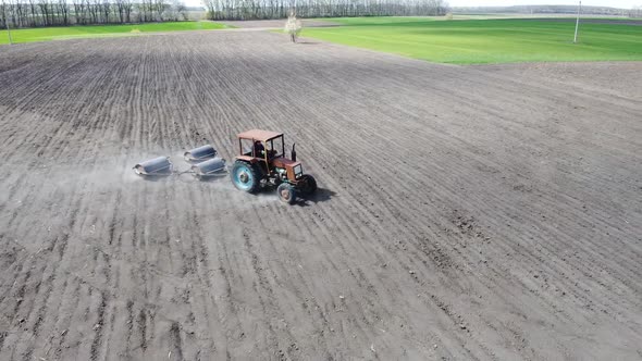 An old rusty tractor entails trailing rollers to tamp the ground on the field after sowing.