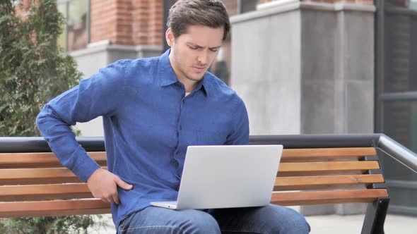 Sitting Outdoor Young Man with Back Pain Working on Laptop alt
