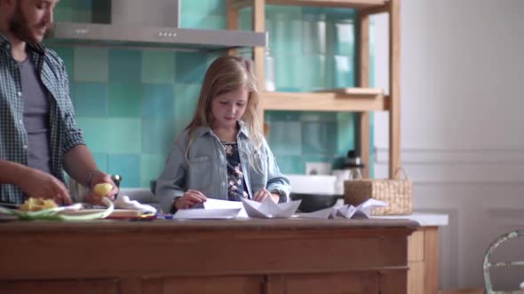 Little girl proudly showing drawing to her father in the kitchen alt