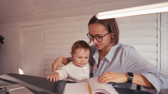 A Young Mother is Working at Home Using Computer While She's Taking Care of Her Baby alt