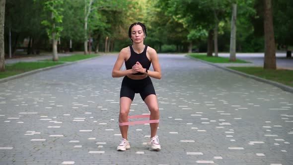 Front View of Stylish Woman with Dreadlocks Makes Crounchy Side Steps with Pink Rubber Band on Legs alt