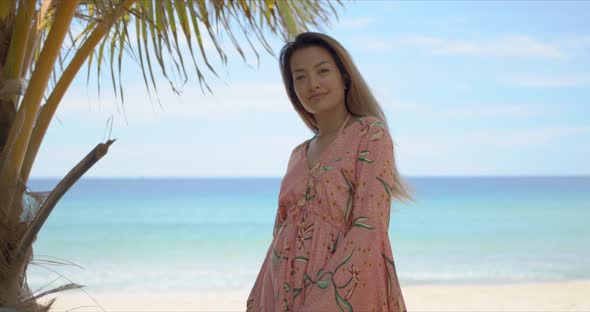 Cheerful Ethnic Female Standing Near Palm on Beach alt