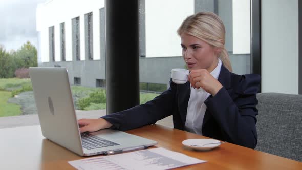 Woman at Lunchtime Communicates on a Laptop and Drinking Coffee alt