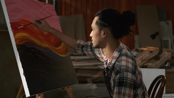 Asian male Artist Draws create art piece with palette and brush painting at studio.