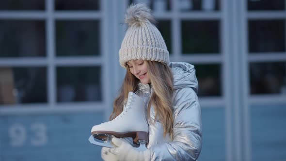 Happy Cute Caucasian Girl Holding Ice Skates Looking at Camera and Smiling alt