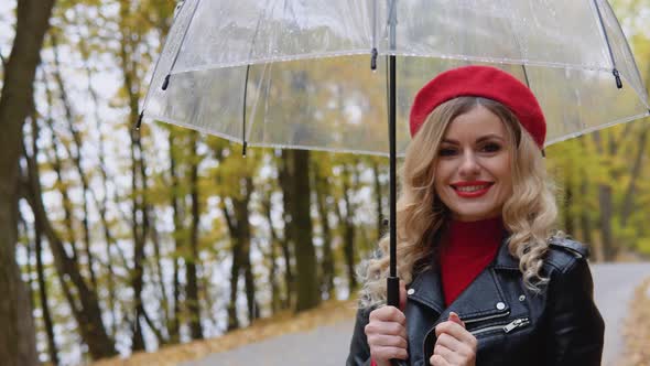 Smiling Happy Cheerful Woman in a Red Suit and a Biker Jacket with a Transparent Umbrella on a Rainy alt