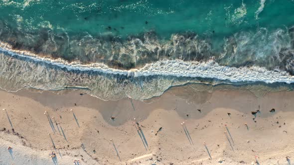 Top down view of vibrant blue waves breaking on a white beach at sunset