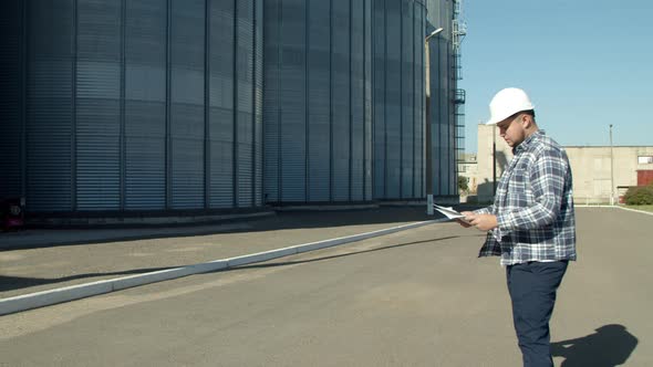 Professional Engineer with Blueprints Inspecting Agricultural Silos