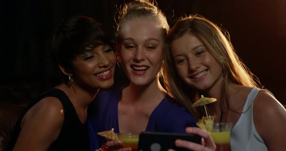 Smiling friends taking a selfie from mobile phone while having cocktail alt