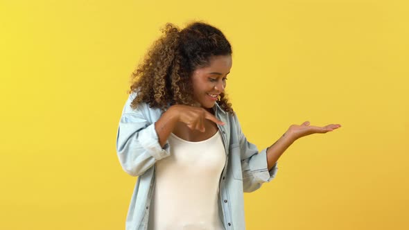 Smiling African American young woman pointing something down with fingers and making ok sign
