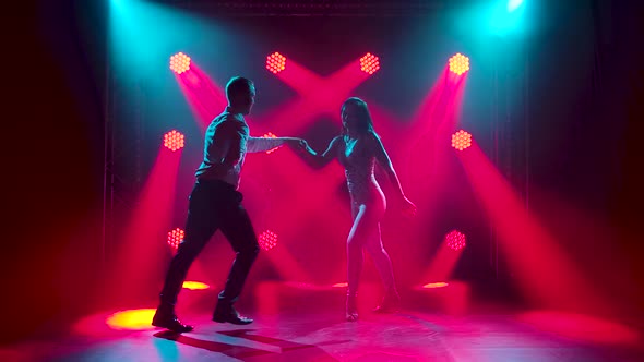 Young Couple Dancing Latin Music. Bachata, Merengue, Salsa. Shot in a Dark Studio with Neon Lights alt