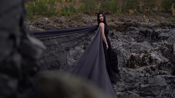 Beautiful Girl with Black Hair Stands in Long Dress on Cliff Mountain alt