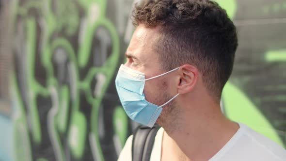 Cute Young Man in a White Tshirt and a Protective Mask in the City on a Graffiti Background alt