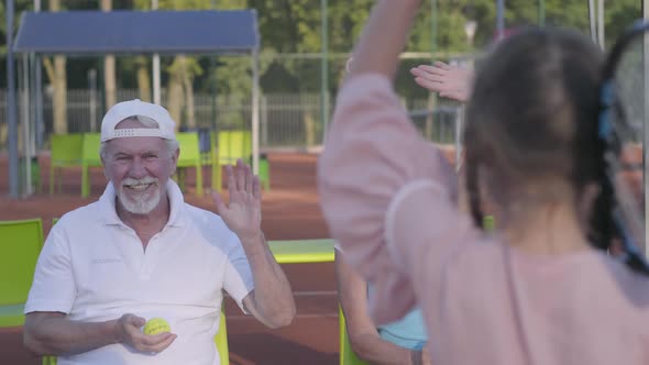 Back View of Cute Funny Girl with Two Pigtails Standing on the Tennis Court Holding Racket alt