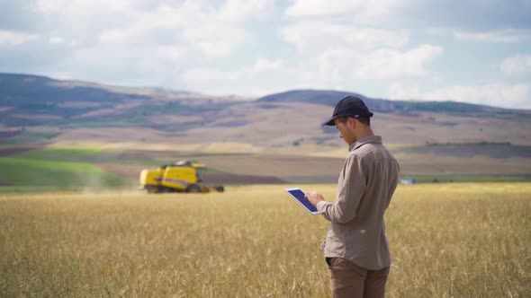 Farmer working with his tablet while the combine machine is harvesting. alt