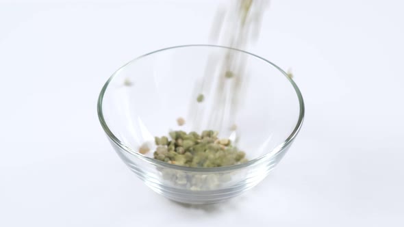 Dry green split peas falling into a glass bowl on white background