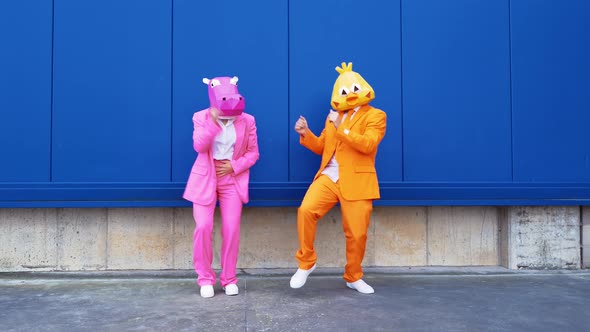 Business couple wearing animal masks dancing in front of blue wall