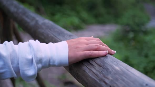 A woman's hand clings to a wooden railing in the woods, she walks away from the camera, slow motion.