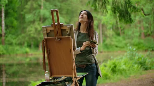 Middle View of a Beautiful Brunette Woman Painting a Picture on Canvas in a Park alt