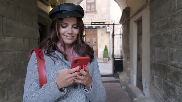 Young Beautiful Girl In Autumn Dress With Dental Braces Sincerely Smiles And Uses A Smartphone.