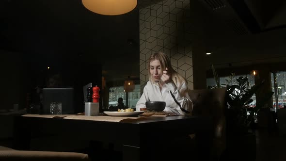 Lonely Blonde Girl Eating Soup Sitting in a Restaurant