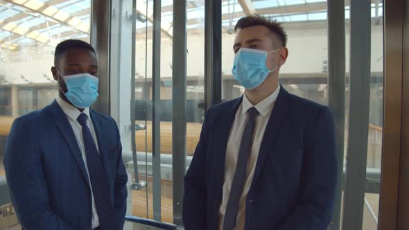 Diverse Employees in Safety Mask Taking Glass Elevator in Business Center alt