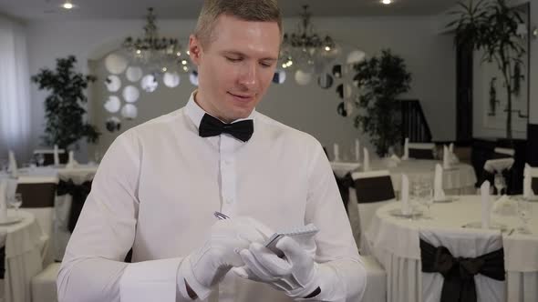 Waiter in a White Shirt and Bow Tie Writing Down an Order in a Cafe Close Up alt