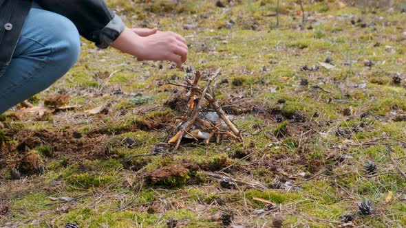 Young Male Making a Small Forest Campfire Using Sticks and Warming Up His Hands alt