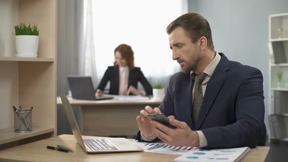 Man in Suit Checking Cellphone, Typing Data on Laptop, Office Work, Distraction alt