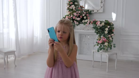 Pretty little girl with long blond hair filming myself on the camera of blue smartphone