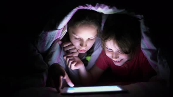 Children Playing Game on Tablet at Night Under Blanket alt