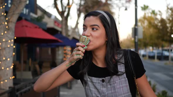 A cute young woman laughing and eating a messy ice cream cone dessert on a city street in slow motio alt