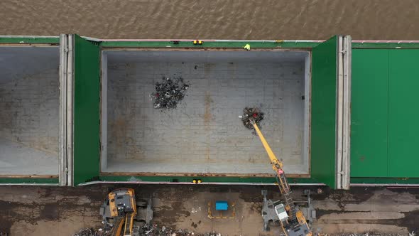 Aerial birdseye footage of mechanical grab machines loading scrap metal onto a ship. alt