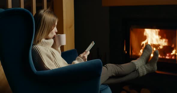 Woman Reads eBook on Electronic Reader By Fireplace in Cozy Room at Night