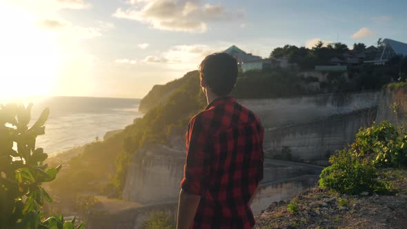 Young Man Traveler Enjoying Beautiful Sunset While Standing on a Rock on a Background of the Sea