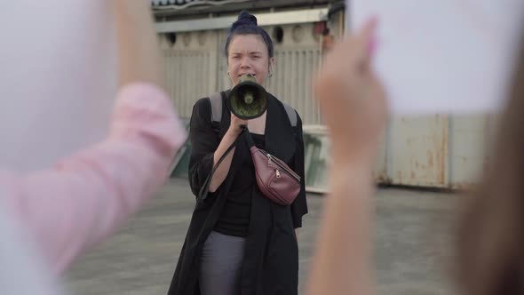 Portrait of Protest Leader Shouting Through Megaphone As Unrecognizable Crowd Shaking Banners alt