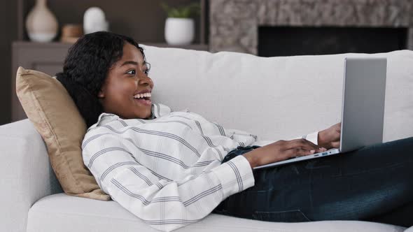 African Emotional Girl American Woman Looking at Laptop Lying on Sofa at Home Feels Delighted alt