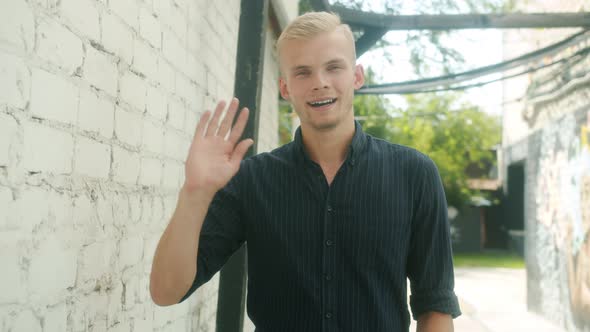 Slow Motion Portrait of Handsome Young Man Waving Hand and Smiling Standing Outside in City Street alt