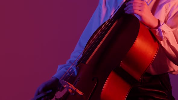 Woman in the Studio Play the Cello with a Bow and Hand on Strings on a Colored Background alt